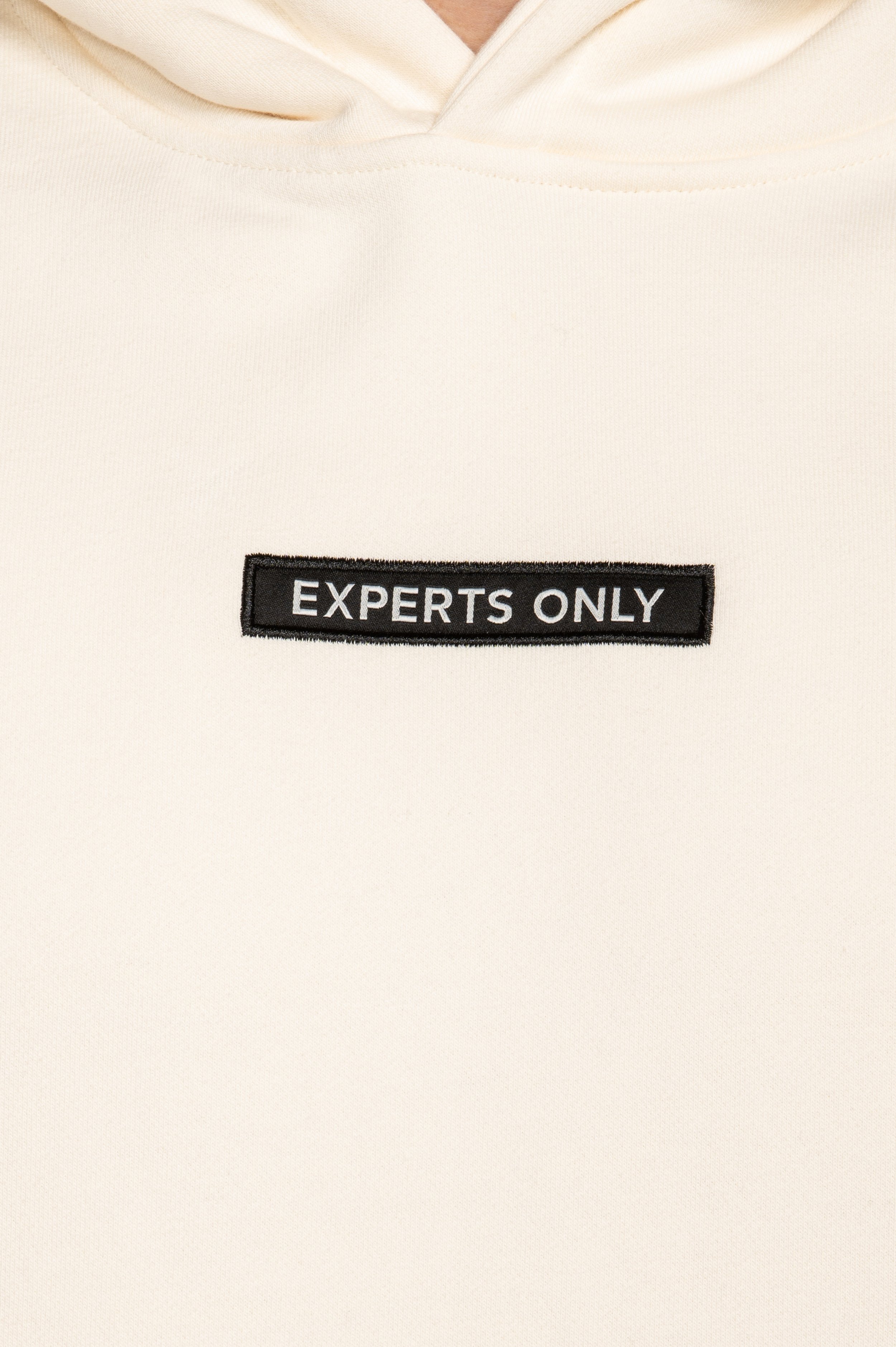 Detailed view of 'Experts Only' front patch on Cream hoodie