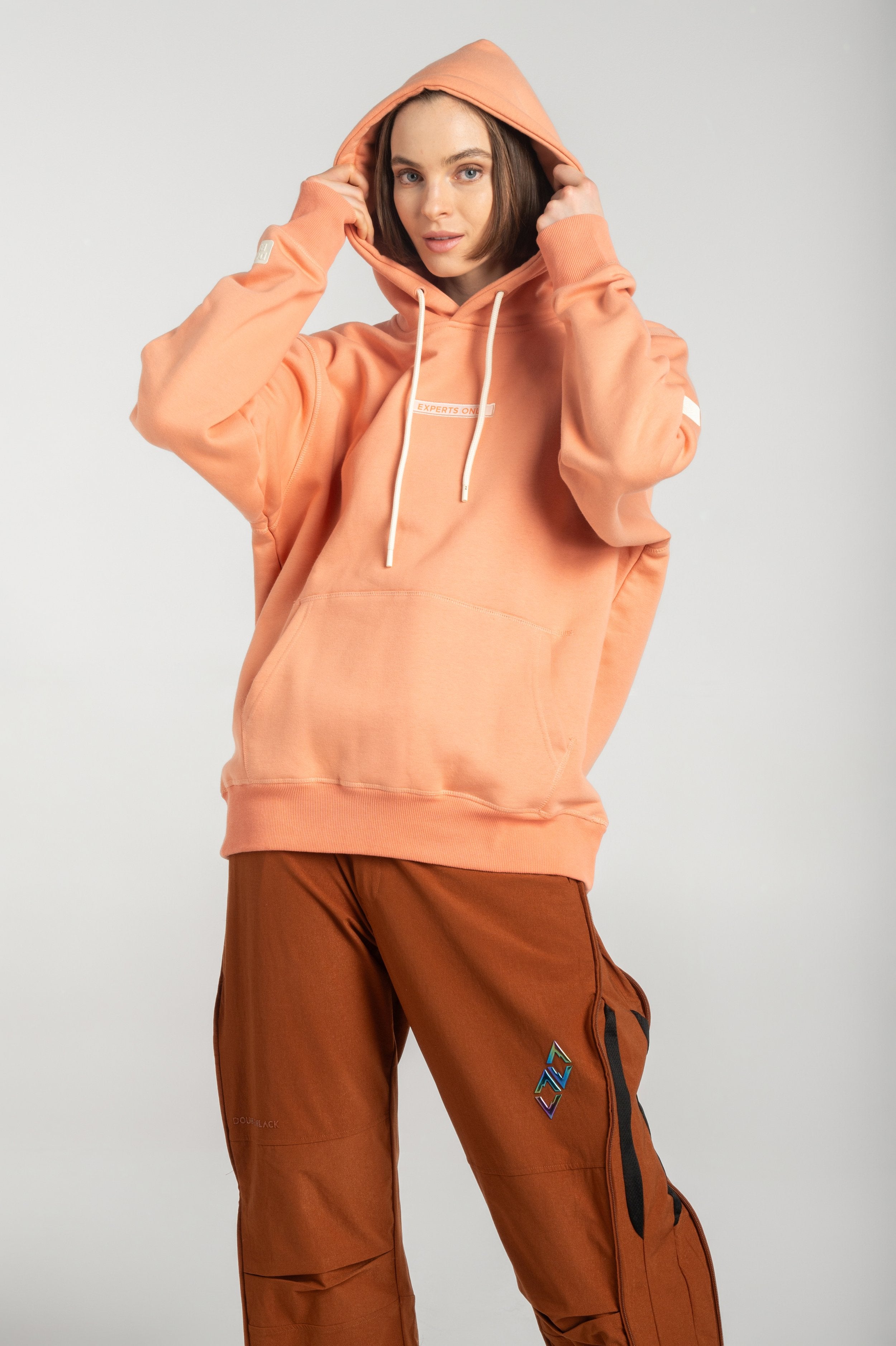 Streetwear styling of Double Black Experts Only hoodie in Salmon – relaxed fit shown with cargo pants